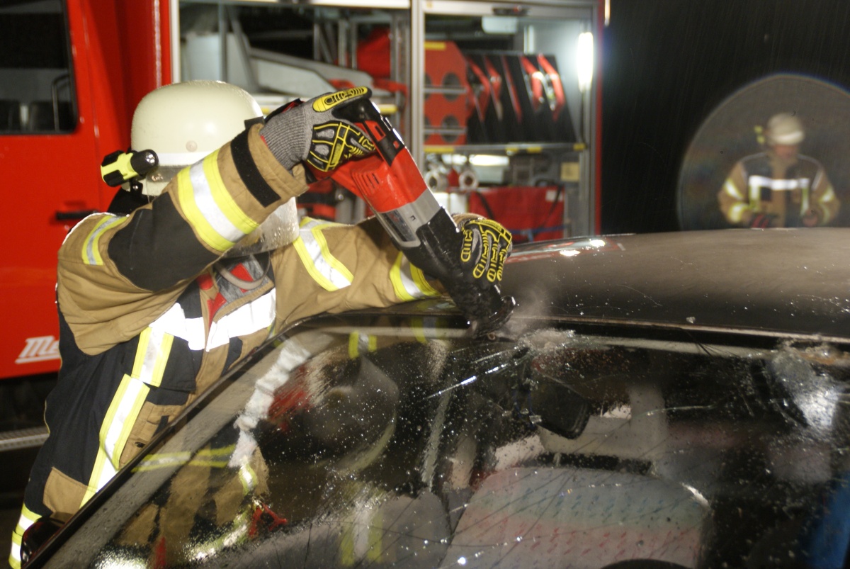 Feuerwehrkamerad schneidet mit Säbelsäge die Frontscheibe aus einem Unfallauto